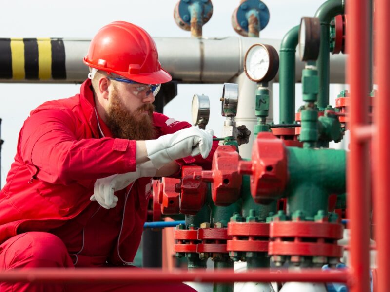 Commercial gas certificates UK Engineer in red overalls, hard hat and safety glasses inspecting pressure gauges and valves during a UK commercial gas safety inspection