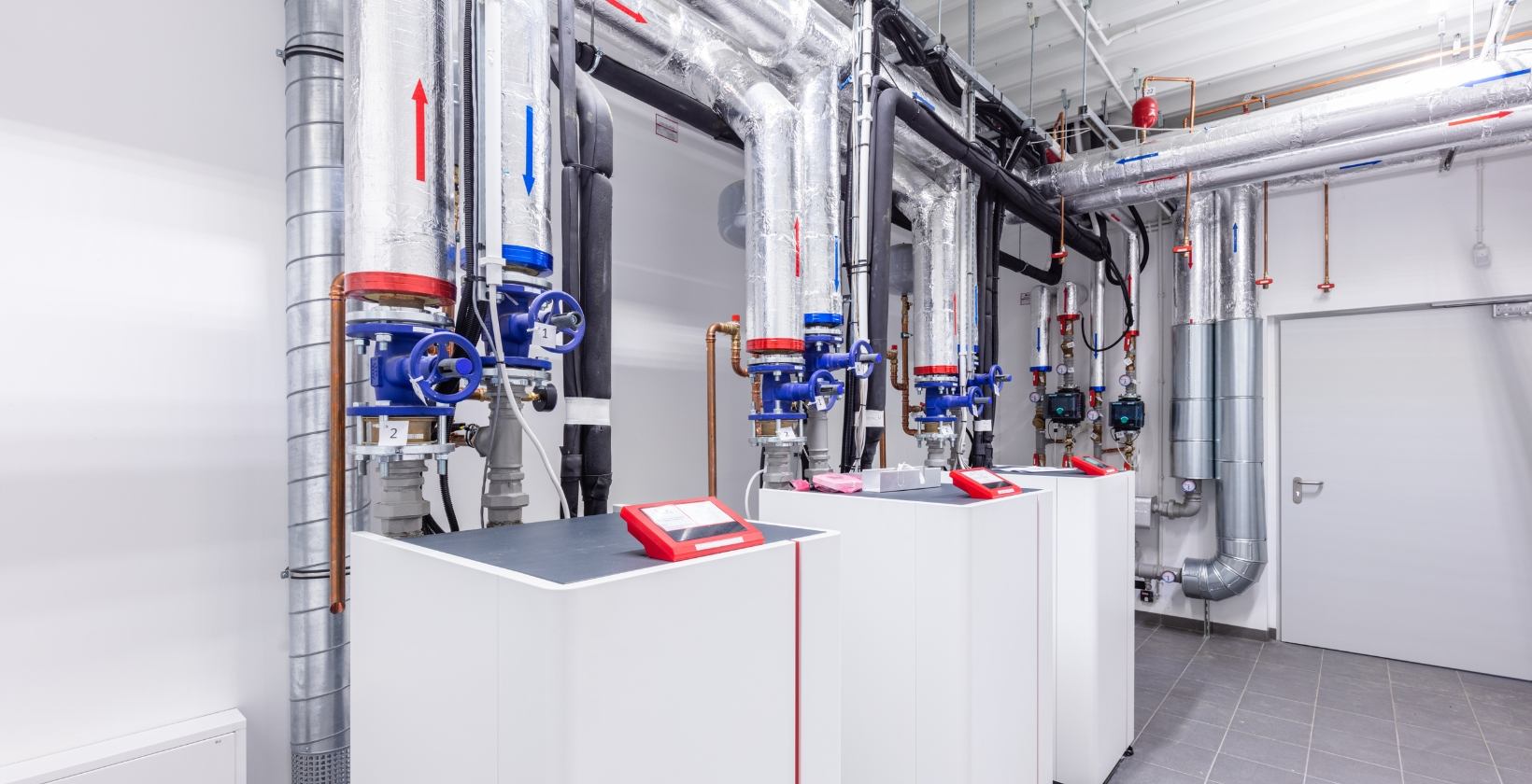 Commercial heating systems UK UK commercial plant room with floor-standing gas boilers, insulated flow and return pipework and blue isolation valves